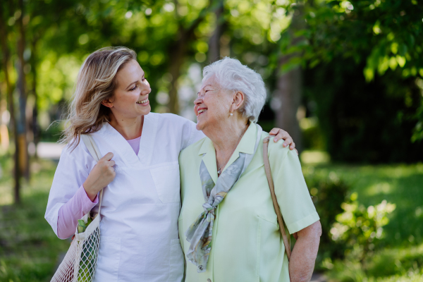 Portrait of caregiver with senior woman on walk in park.