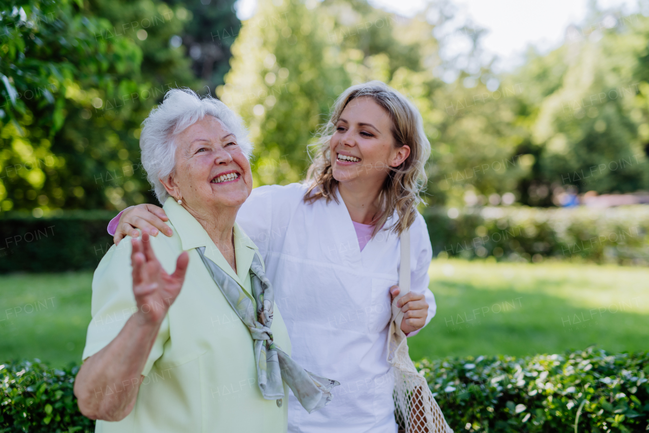 A portrait of caregiver with senior woman on walk in park with shopping bag, laughing and talking.