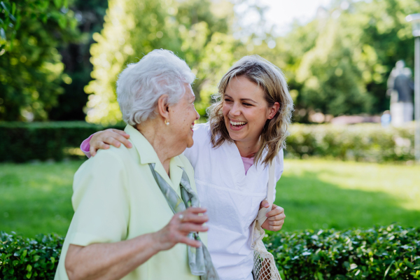 Portrait of caregiver with senior woman on walk in park.