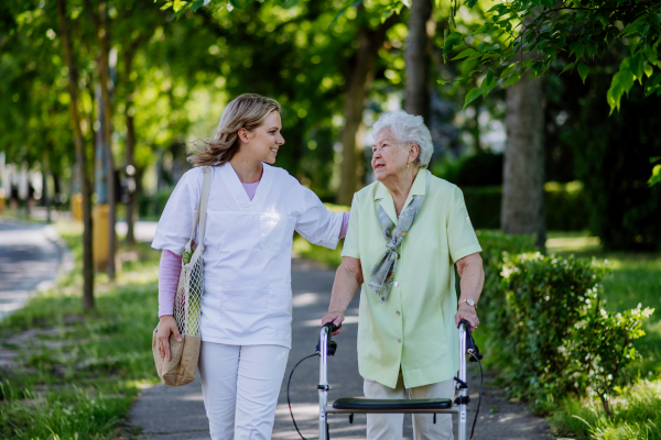 Portrait of caregiver with senior woman on walk in park.