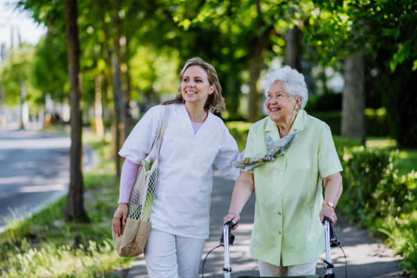 Portrait of caregiver with senior woman on walk in park.