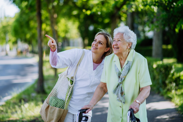 Portrait of caregiver with senior woman on walk in park.