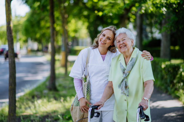 Portrait of caregiver with senior woman on walk in park.