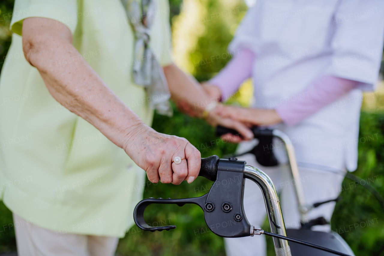 A close-up of caregiver helping senior woman on walk with walker in park.