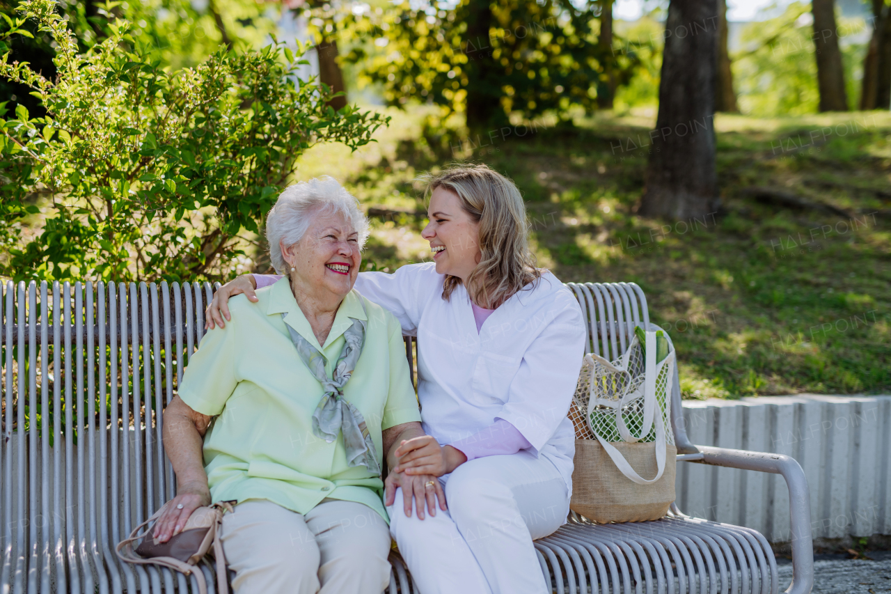 Caregiver with senior woman sitting on bench in park in summer, and talking with senior woman.