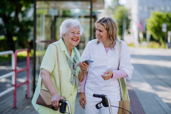 A portrait of caregiver with senior woman on walk in park with shopping bag, laughing and talking.