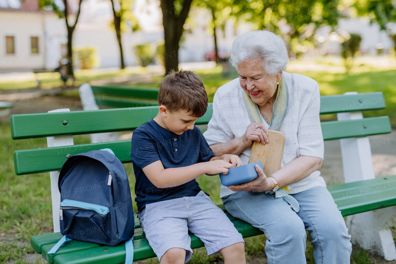 A great grandmother sitting on bench with her grandson and eating healthy fruit snack together, generation family concept.