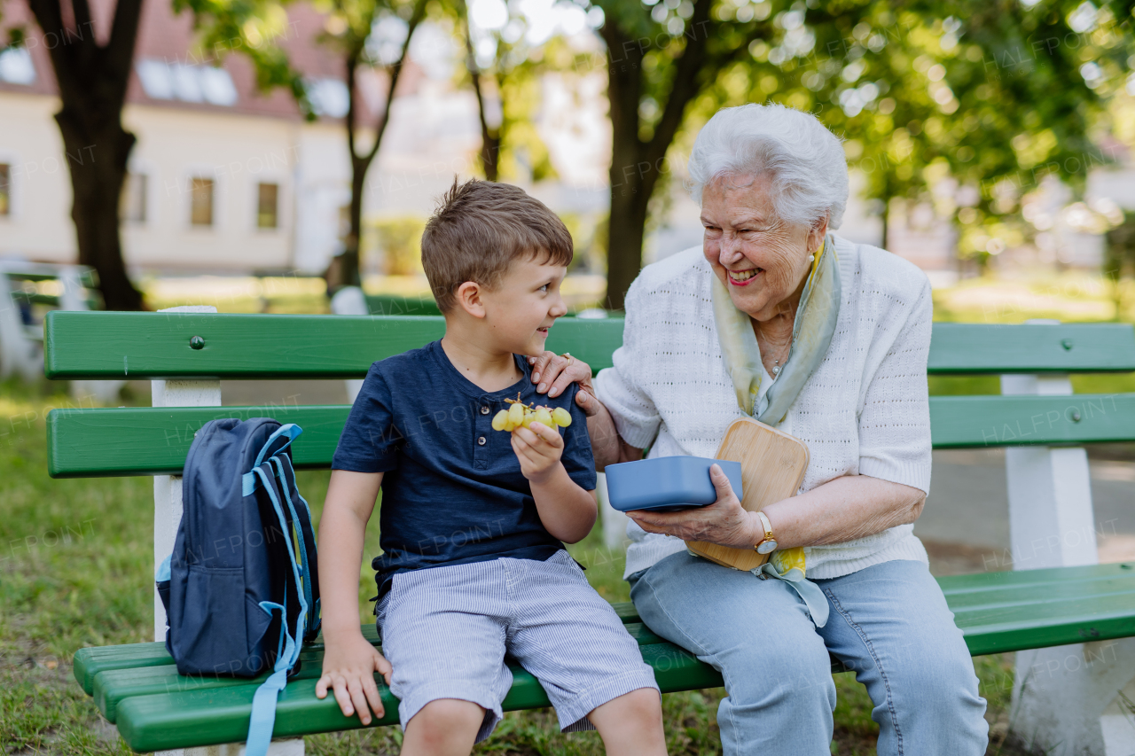 A great grandmother sitting on bench with her grandson and eating healthy fruit snack together, generation family concept.