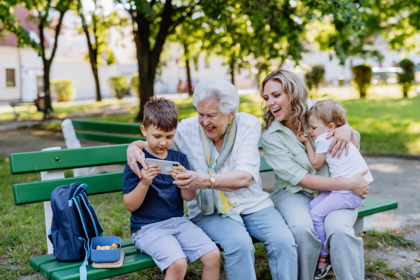 A great grandmother taking selfie with her granddaughter and kids when sitting in park in summer.