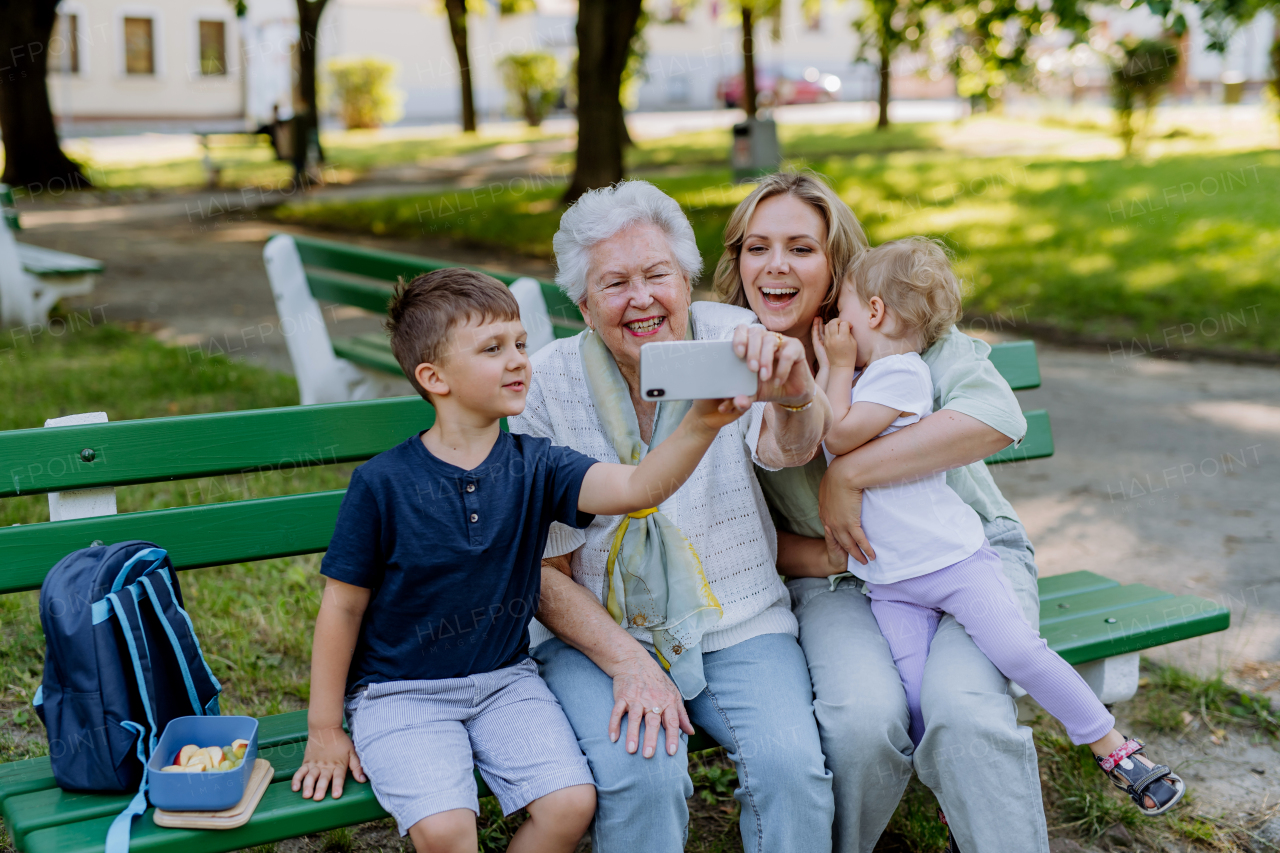 A great grandmother taking selfie with her granddaughter and kids when sitting in park in summer.