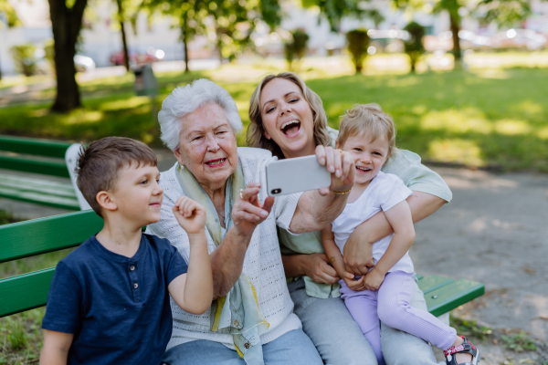 A great grandmother taking selfie with her granddaughter and kids when sitting in park in summer.