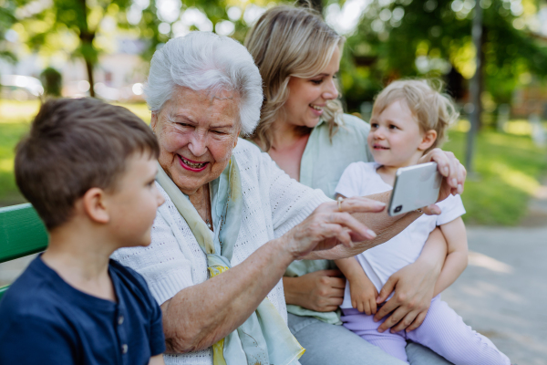 A great grandmother taking selfie with her granddaughter and kids when sitting in park in summer.