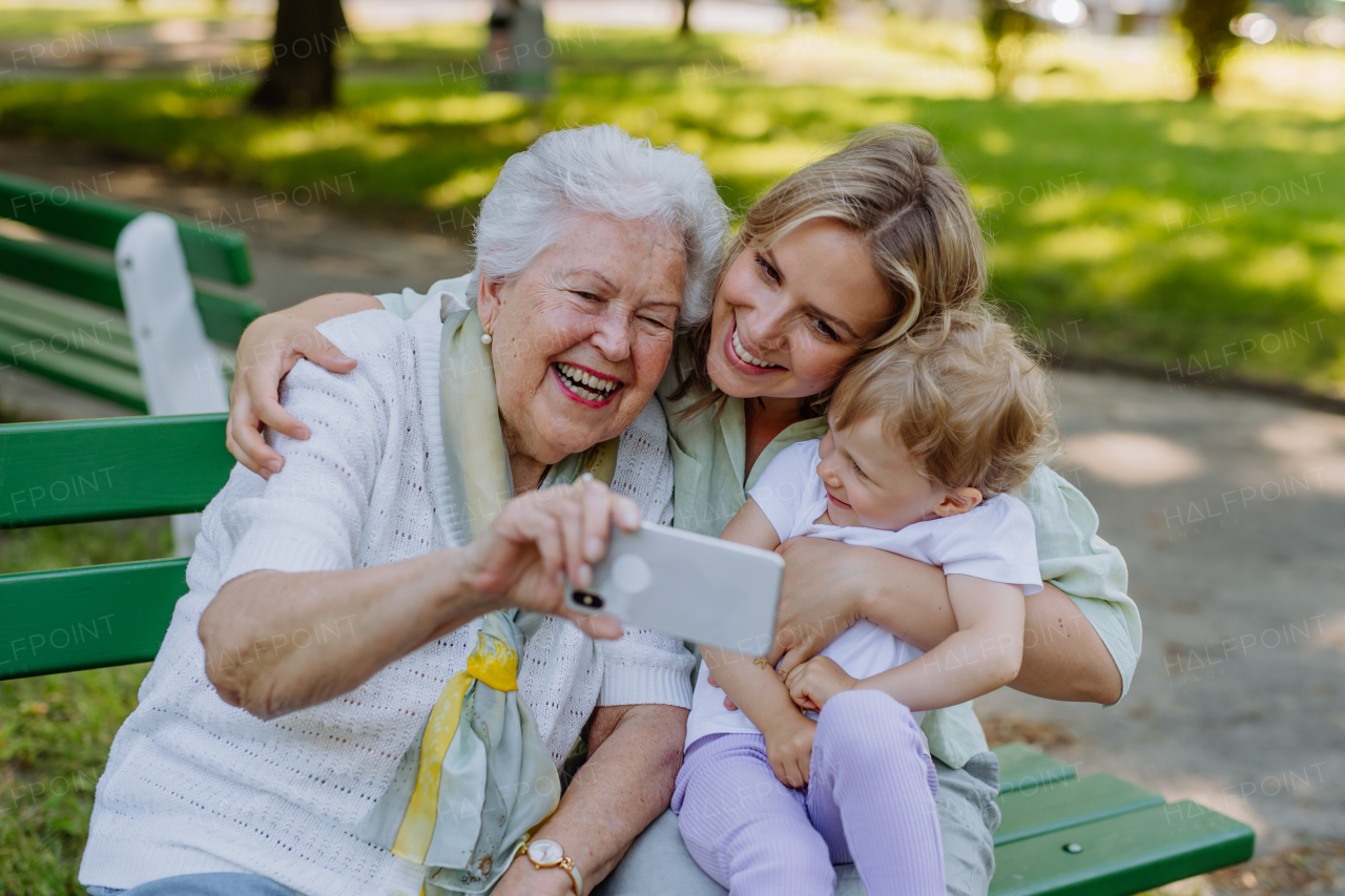 A great grandmother taking selfie with her granddaughter and kid when sitting in park in summer.