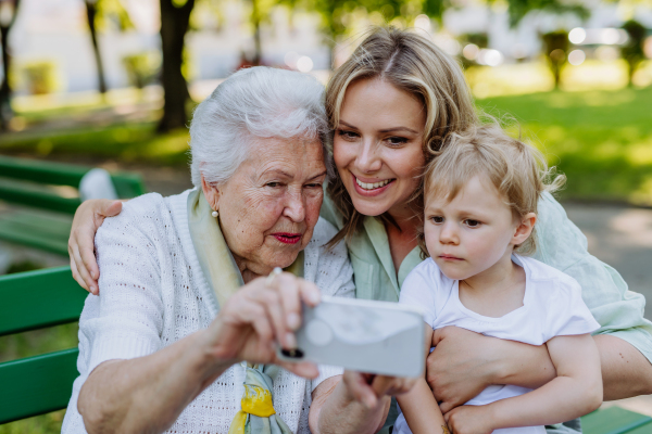 A great grandmother taking selfie with her granddaughter and kid when sitting in park in summer.