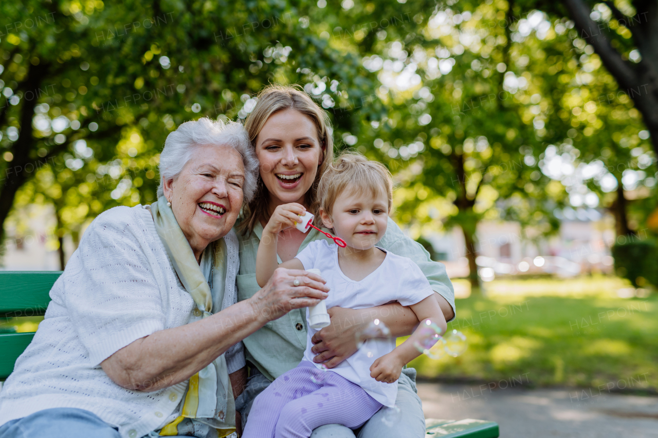 A happy smiling woman with senior grandmother and little daughter blowing soap bubbles at park, family, generation and people concept.