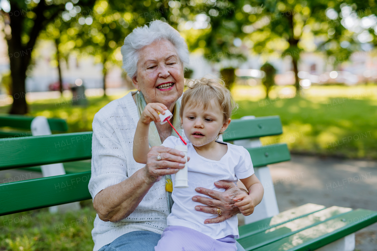 A great grandmother sitting on bench with her granddaughter and blowing soap bubbles together, generation family concept.