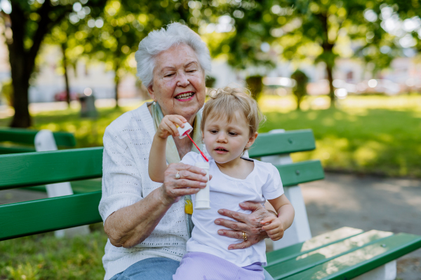 A great grandmother sitting on bench with her granddaughter and blowing soap bubbles together, generation family concept.