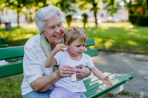 A great grandmother sitting on bench with her granddaughter and blowing soap bubbles together, generation family concept.