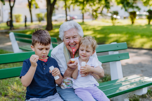 A great grandmother sitting on bench with her grandchildren and blowing soap bubbles together, generation family concept.