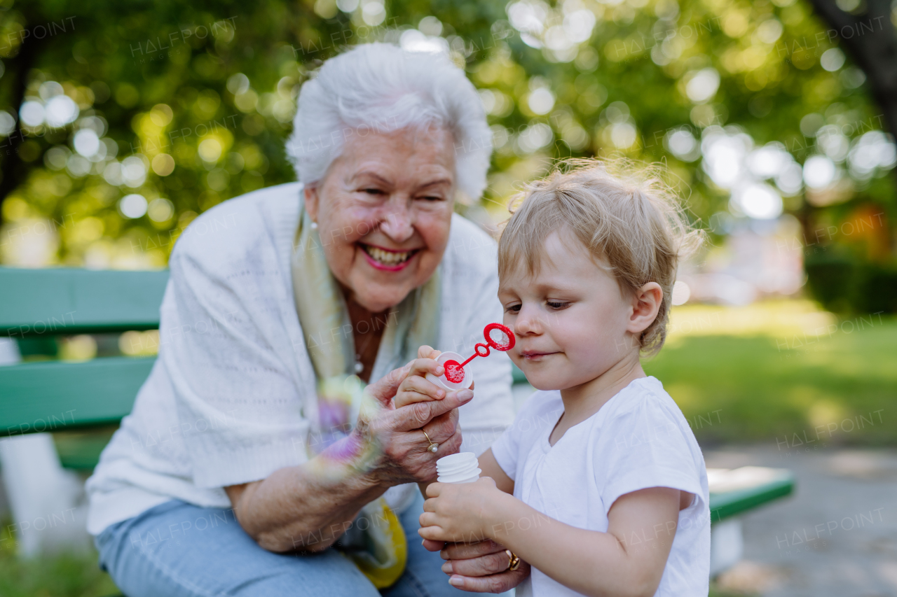 A great grandmother sitting on bench with her granddaughter and blowing soap bubbles together, generation family concept.