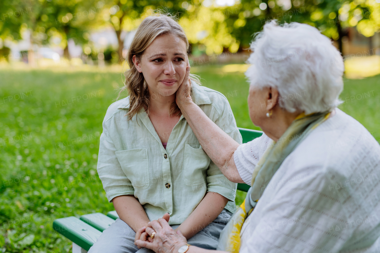 A worried senior grandmother comforting grown up granddaughter when sitting on bench in park, share problem with someone close concept