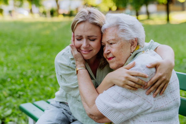 A worried senior grandmother comforting grown up granddaughter when sitting on bench in park, share problem with someone close concept