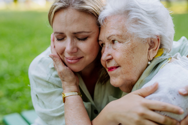 A worried senior grandmother comforting grown up granddaughter when sitting on bench in park, share problem with someone close concept