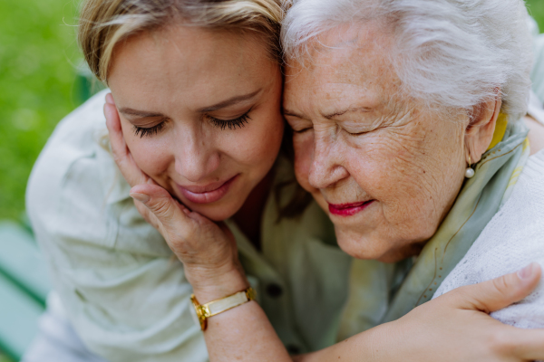 A close up of grownup granddaughter and senior grandmother cuddling, enjoying tender moment, hugging, expressing love,sittingon bench in park.