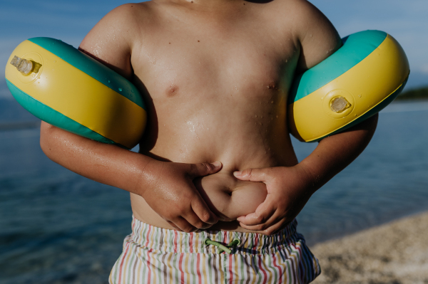 Boy in swimsuit at beach holding his belly fat, body shaming young childrens.