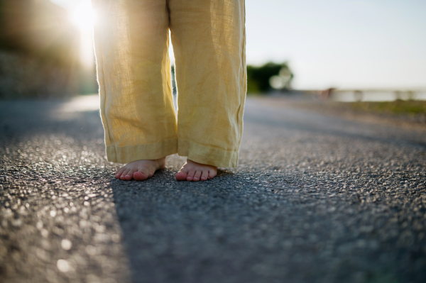 Close up of girl's barefoot legs in summer outfit on walk during summer vacation, wearing yellow linen pants.