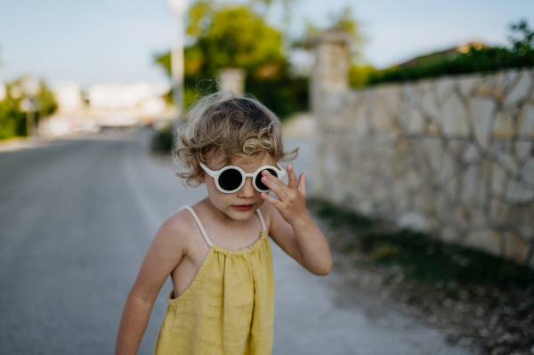 Portrait of blonde girl in summer outfit and sunglasses on walk during summer vacation, concept of beach holiday.