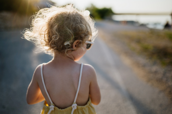 Rear view of blonde girl in summer outfit on walk during summer vacation, beach holiday.