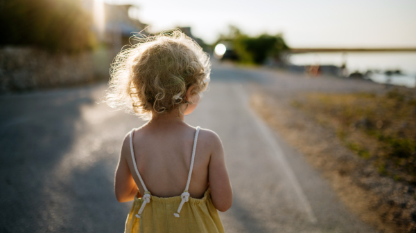 Rear view of blonde girl in summer outfit on walk during summer vacation, beach holiday.