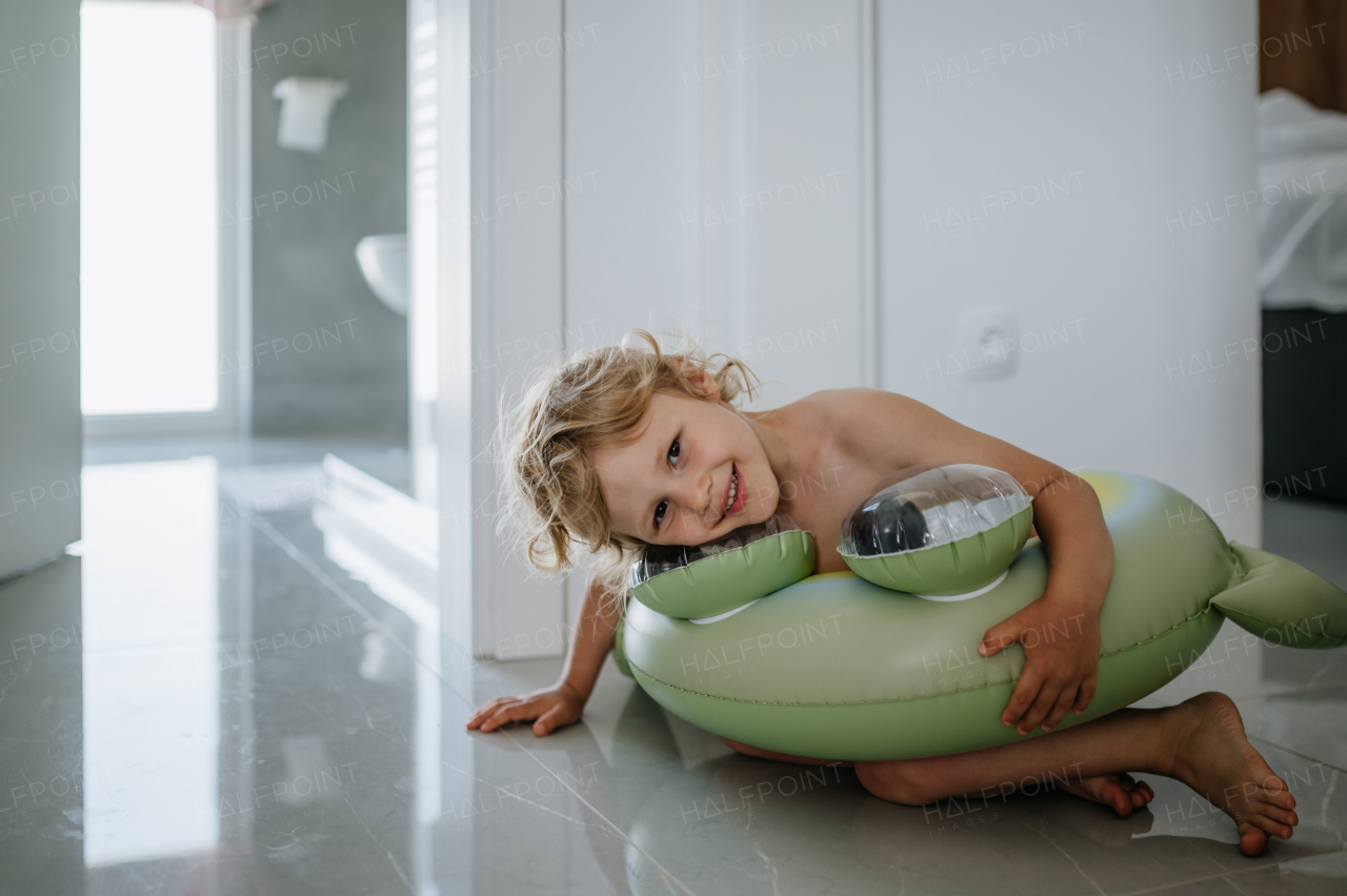 Small girl is excited to go on the beach. Standing in living room in swimsuit and inflatable toy ring.