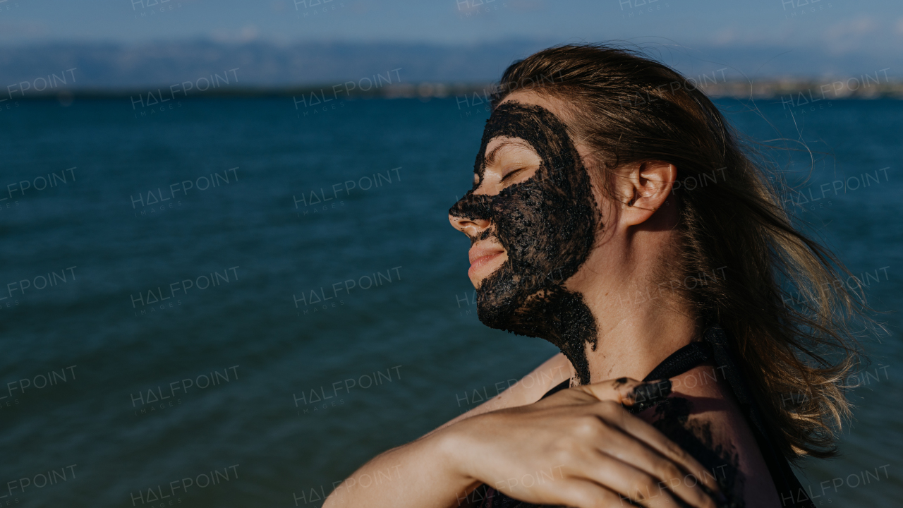 Woman applies healing mud to her face and body. Natural healing mud in Croatia on the beach. Therapeutic mud or peloids rich in minerals and organic substances.