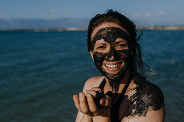 Woman applies healing mud to her face and body. Natural healing mud in Croatia on the beach. Therapeutic mud or peloids rich in minerals and organic substances.