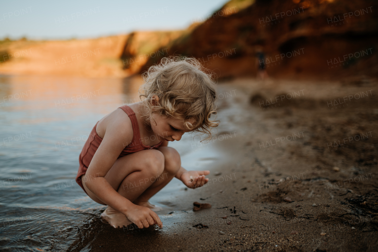 Small girl in swimsuit playing at beach, crouching and seraching for shells in the sand.