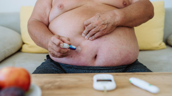 Overweight man with diabetes injecting insulin in his abdomen. Close up of man with type 1 diabetes taking insuling with insuling pen.