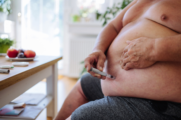 Overweight man with diabetes injecting insulin in his abdomen. Close up of man with type 1 diabetes taking insuling with insuling pen.