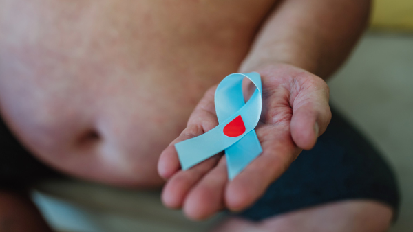 Overweight man holding a blue diabetes support ribbon as a symbol of diabetes awareness. November as Diabetes Awareness Month. 14 November as World Diabetes Day.