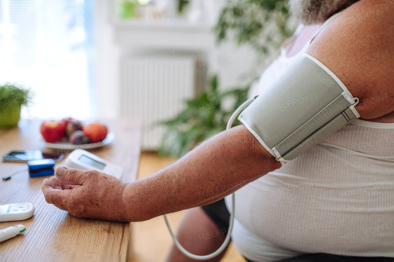 Overweight man measuring his blood pressure at home. Man with high blood pressure using at-home blood pressure monitor.