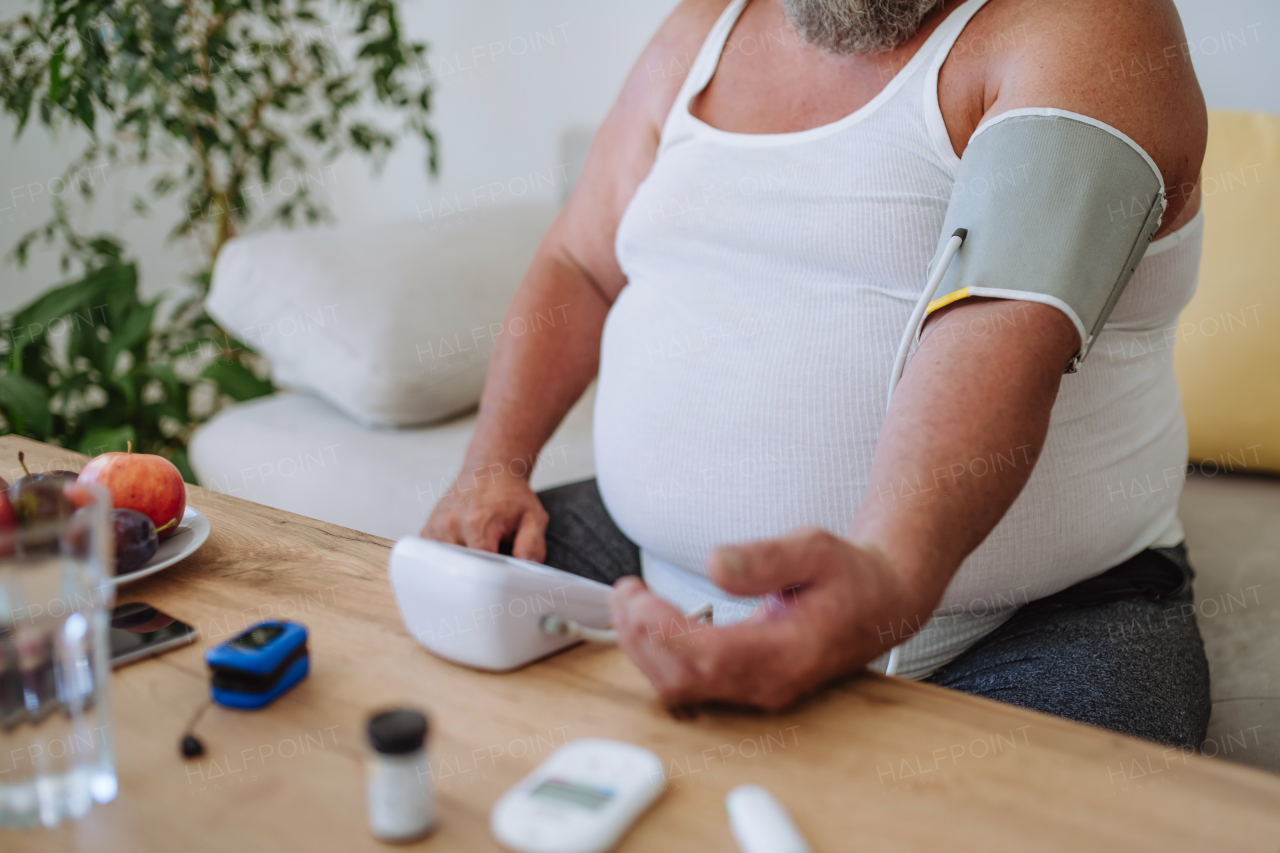 Overweight man measuring his blood pressure at home. Man with high blood pressure using at-home blood pressure monitor.