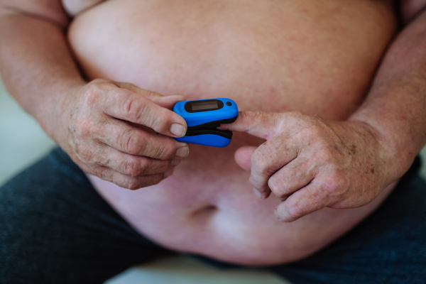 An overweight man is using a pulse oximeter at home to measure blood oxygen saturation.