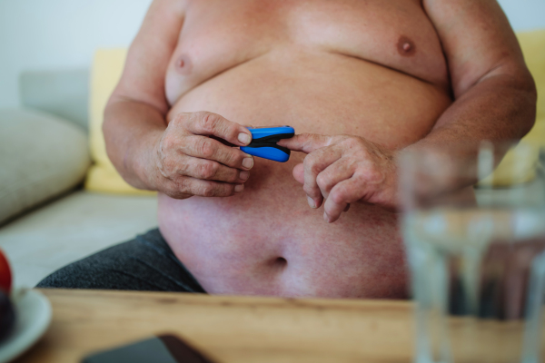 An overweight man is using a pulse oximeter at home to measure blood oxygen saturation.