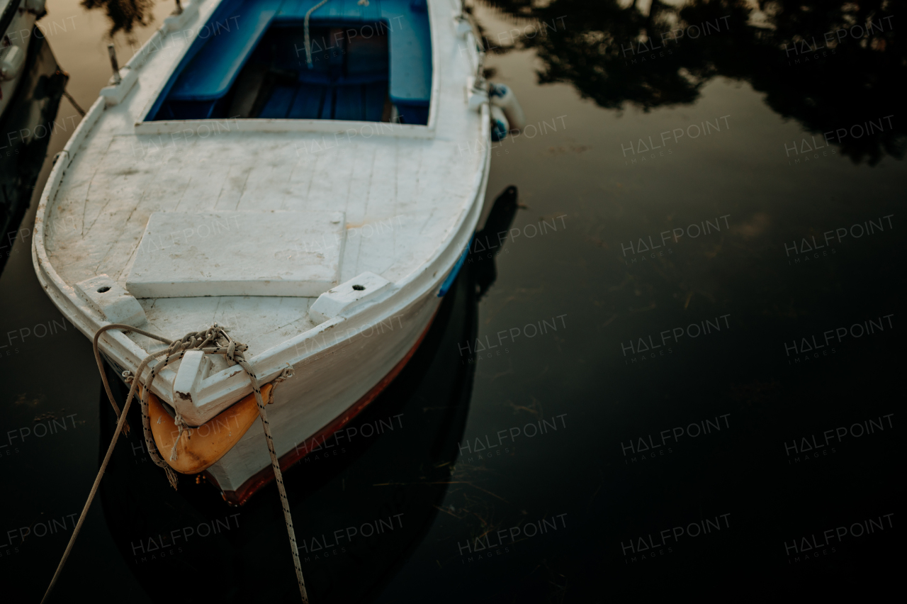 A small boat on calm water, moored in the harbor, dock during sunset.