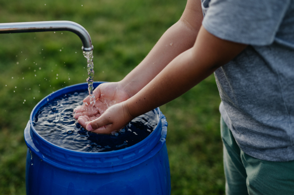 Boy washing his hands with water from a well. Well with a pump for outdoor washing in the garden.