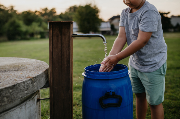 Boy washing his hands with water from a well. Well with a pump for outdoor washing in the garden.