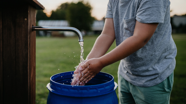 Boy washing his hands with water from a well. Well with a pump for outdoor washing in the garden.