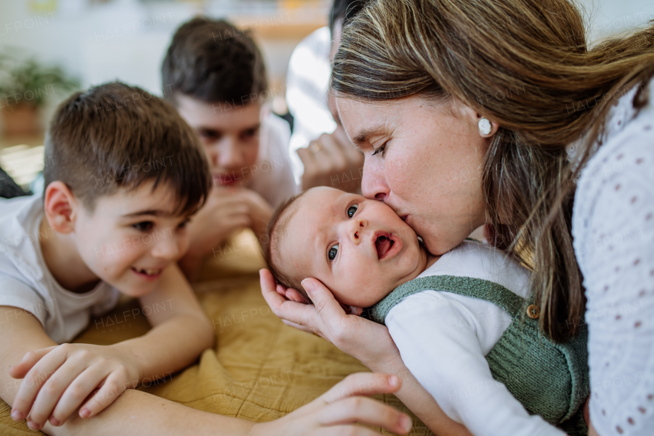 Portrait of woman kissing her newborn baby,other siblings stoking him.