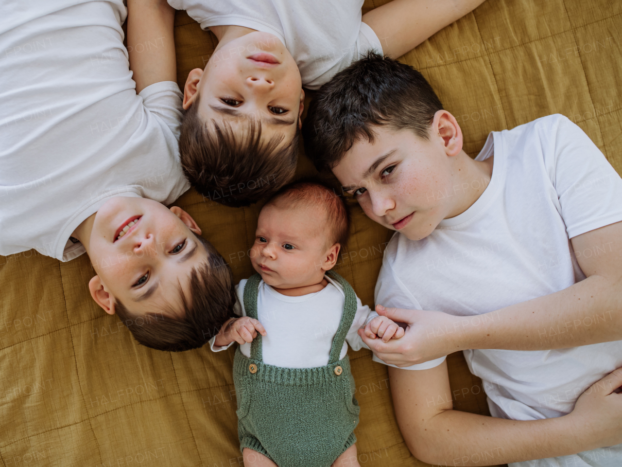 Three big brothers with their newborn brother lying in a bed.